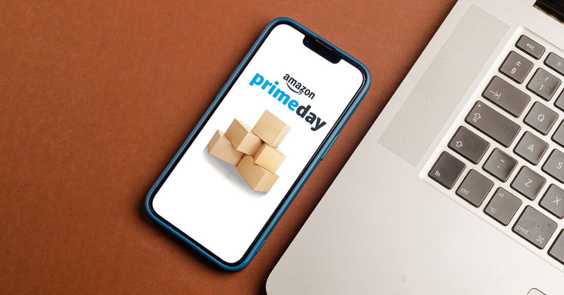 a smartphone displaying a Prime Day announcement, next to a laptop, on a wooden table