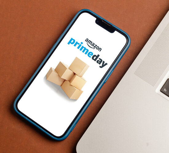 a smartphone displaying a Prime Day announcement, next to a laptop, on a wooden table